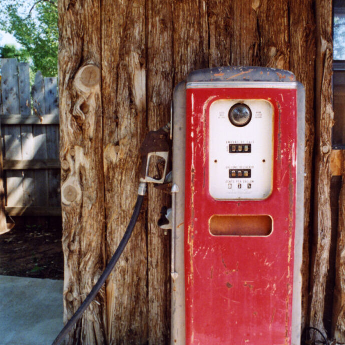 Red painted weathered vintage gasoline pump displayed against rustic log wall.